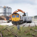 Head on shot of aggregates train being loaded by mechanical shovel with Industrial buildings in the background