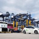 A ground level image of a clean fuel electric car and a tractor in front of dock cranes at Hutchison's Port of Felixstowe
