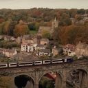A passenger train crosses a viaduct over a town in the north of England countryside