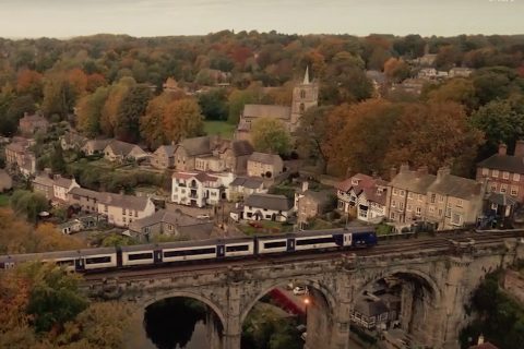 A passenger train crosses a viaduct over a town in the north of England countryside