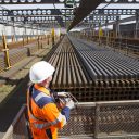 Orange saftey suited engineer inspects stockpile of new rails at British Steel works in UK