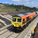 Freightliner class 66 diesel in orange livery pulling away from Buxton quarry in the English Peak District
