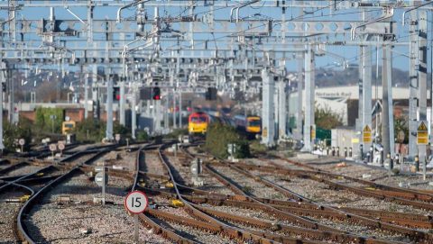 under a tangle of overhead wires a freight train approaches in the distance