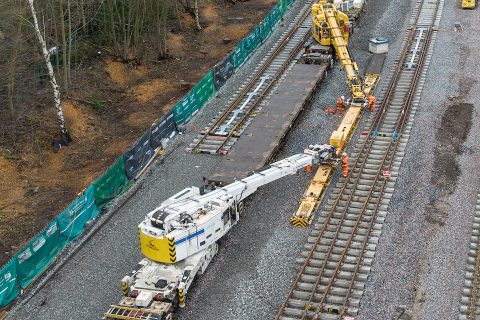 From above, two heavy rail-mounted cranes lower a track section into place